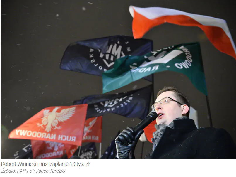 Foto von Robert Winnicki als Redner bei einer Veranstaltung der neofaschistischen Organisation Ruch Narodowy und der von Facebook gebannten neofaschistischen Organisationen ONR und MW. Alle drei Organisationen sind an den entsprechenden Flaggen im Hintergrund hinter Winnicki erkennbar.