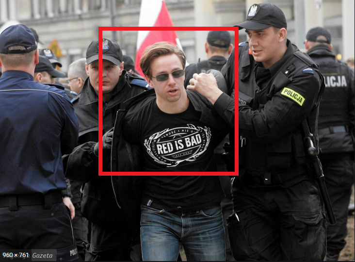 Foto von Krzysztof Bosak, der Vize-Vorsitzende des neofaschistischen Ruch Narodowy, der von zwei Polizisten abgeführt wird. Er trägt dabei ein schwarzes T-Shirt mit dem Logo der in der rechtsextremen Szene beliebten Modelabels "Red is Bad".
